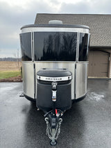 A sleek silver Airstream travel trailer, ideal for an RV rental. Parked on a wet driveway, reflecting trees and a house.