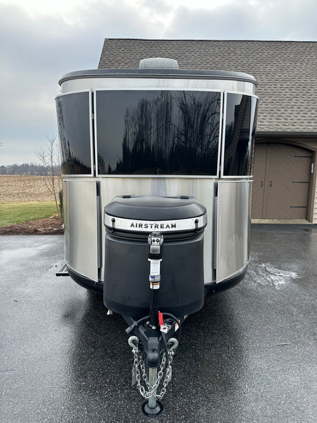 A sleek silver Airstream travel trailer, ideal for an RV rental. Parked on a wet driveway, reflecting trees and a house.