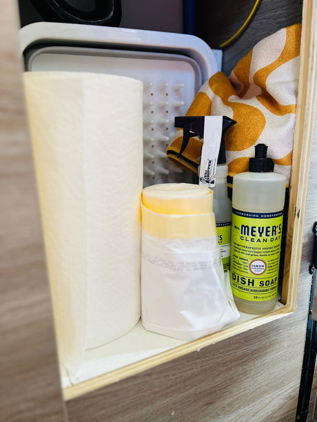 RV rental kitchen essentials: paper towels, Mrs. Meyer's dish soap, a spray cleaner, and a drying rack neatly stored.