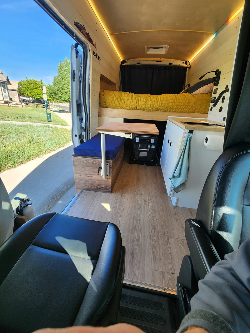 Step into this cozy RV rental camper van: bed, dinette, and kitchen. Wood-paneled interior, with an open door looking outside. — photo 10