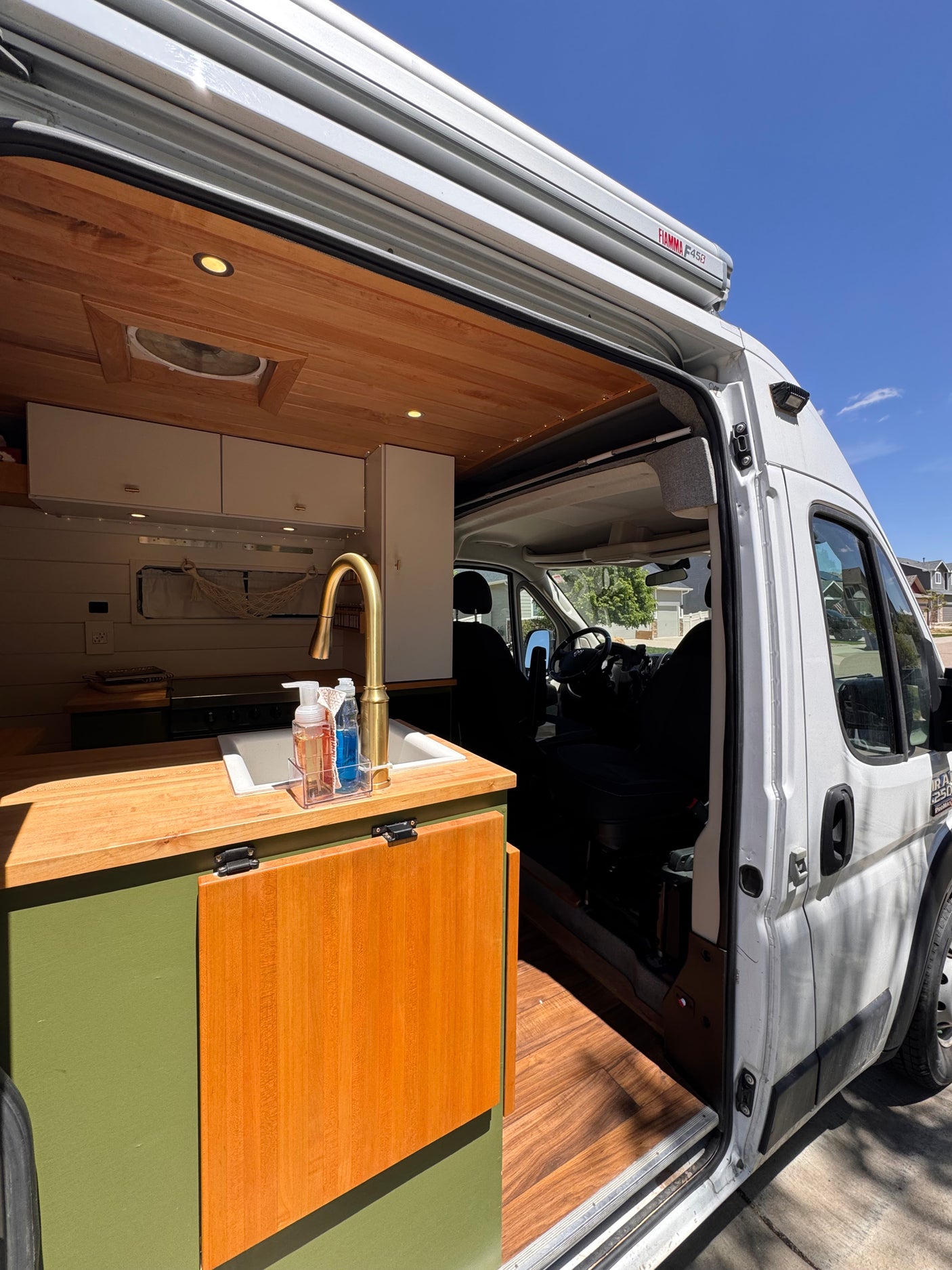 An open-door view inside an RV rental camper van, revealing a custom kitchen with wood counters, a gold faucet, and green cabinets.