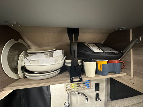 RV rental compact kitchen: stacked dishes, mugs, and a sink with faucet below, showcasing efficient storage for travel.