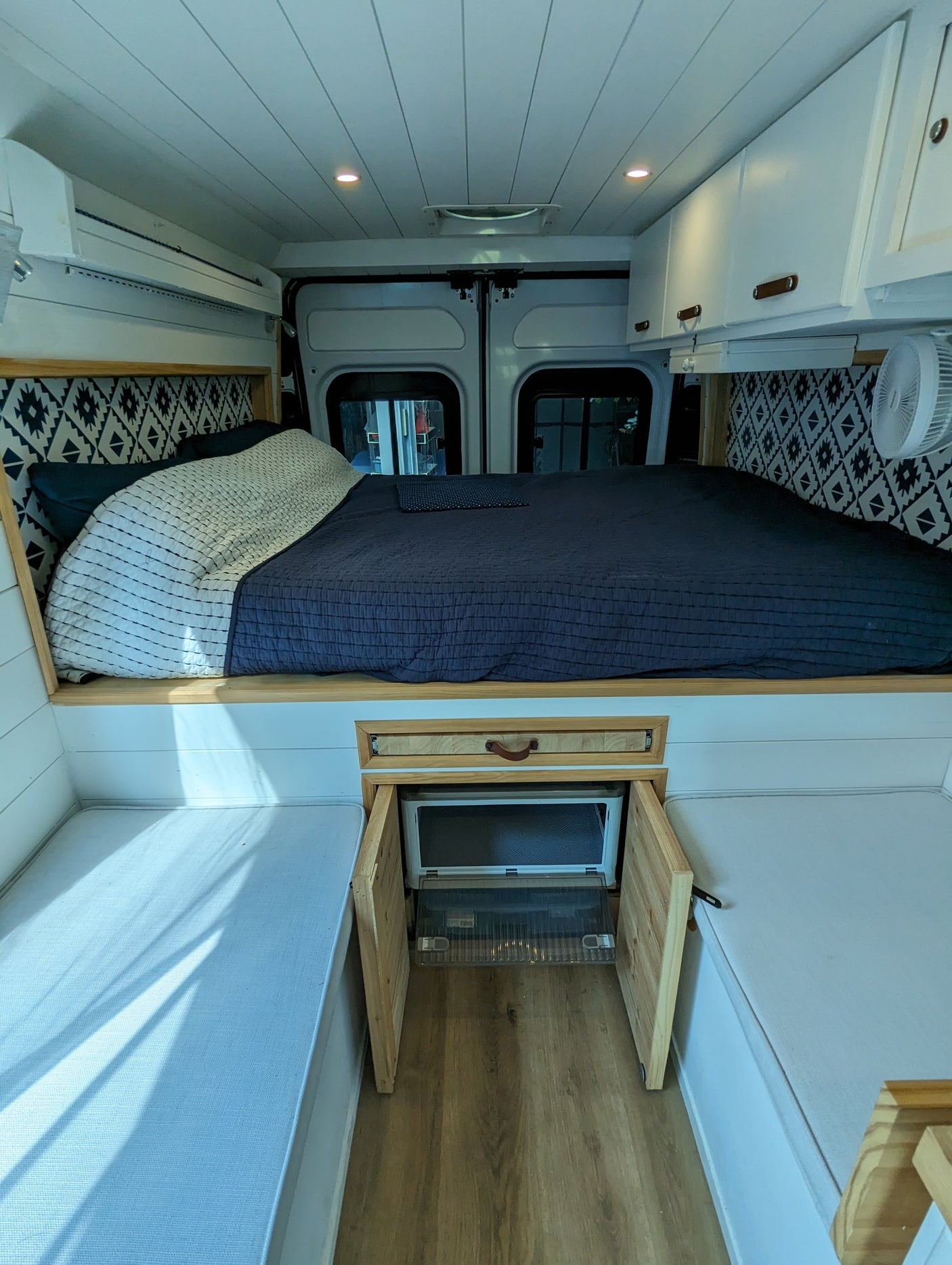 Cozy RV rental interior featuring a raised bed with patterned headboard, integrated fridge, and side bench seating.