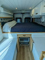 Cozy RV rental interior featuring a raised bed with patterned headboard, integrated fridge, and side bench seating.