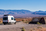 An RV rental van pauses at the entrance to Lake Mead National Recreation Area, with vast desert mountains behind.
