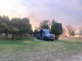 RV rental van parked at a twilight campsite, surrounded by trees. Perfect for outdoor adventures and van life.