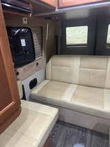 Cozy light-colored seating, a wall-mounted TV, and blinds on the window in this inviting RV rental interior.