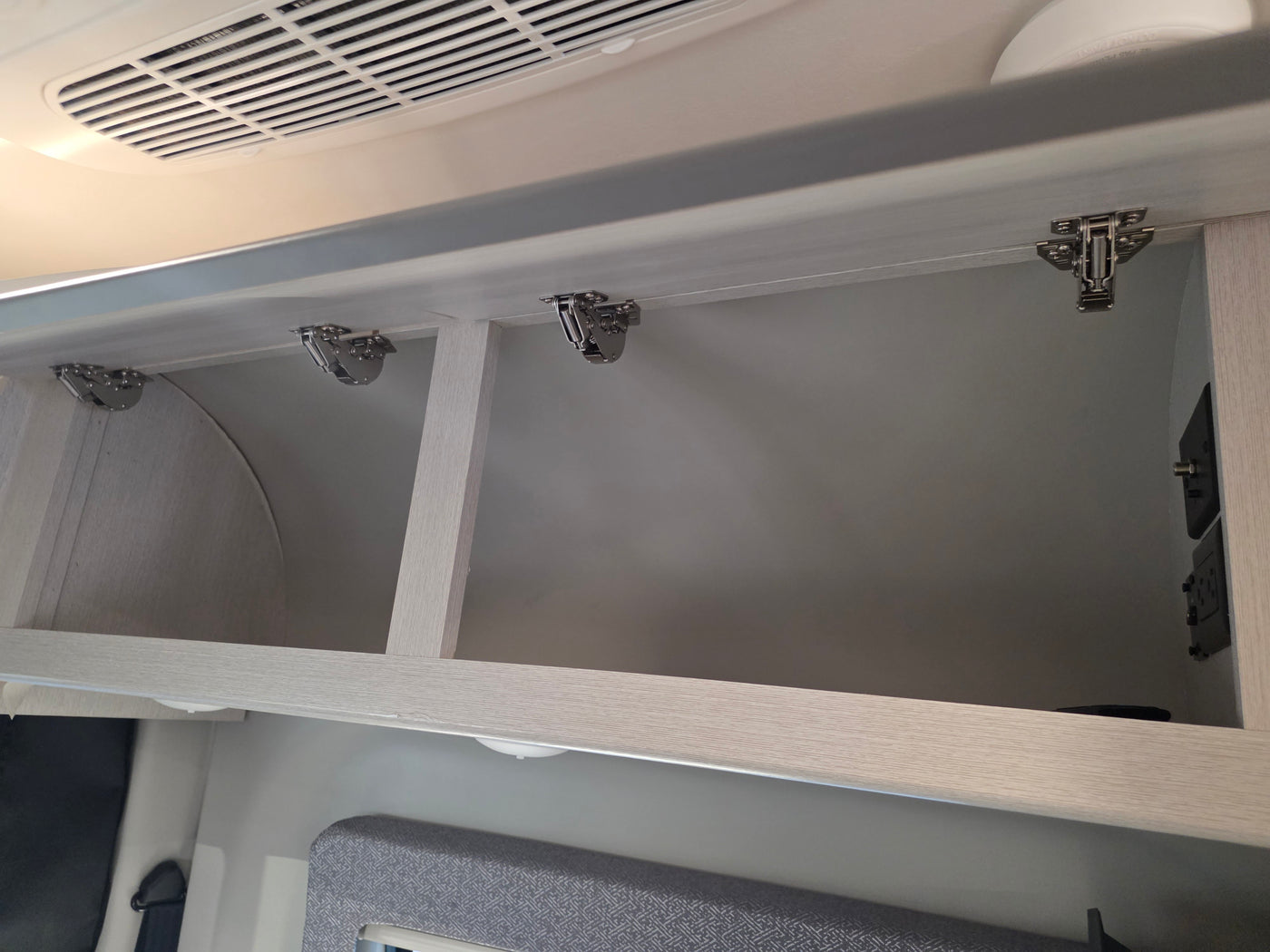 Open overhead cabinets in an RV rental, showing hinges, an air vent, and power outlets for convenient storage. — photo 16