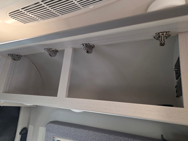 Open overhead cabinets in an RV rental, showing hinges, an air vent, and power outlets for convenient storage. — photo 16