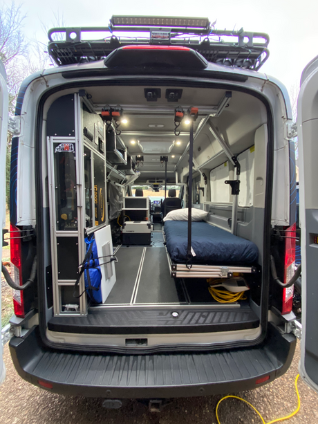 Detailed view of a versatile RV rental camper van's rear interior, featuring a bed, organized storage, and utility gear.