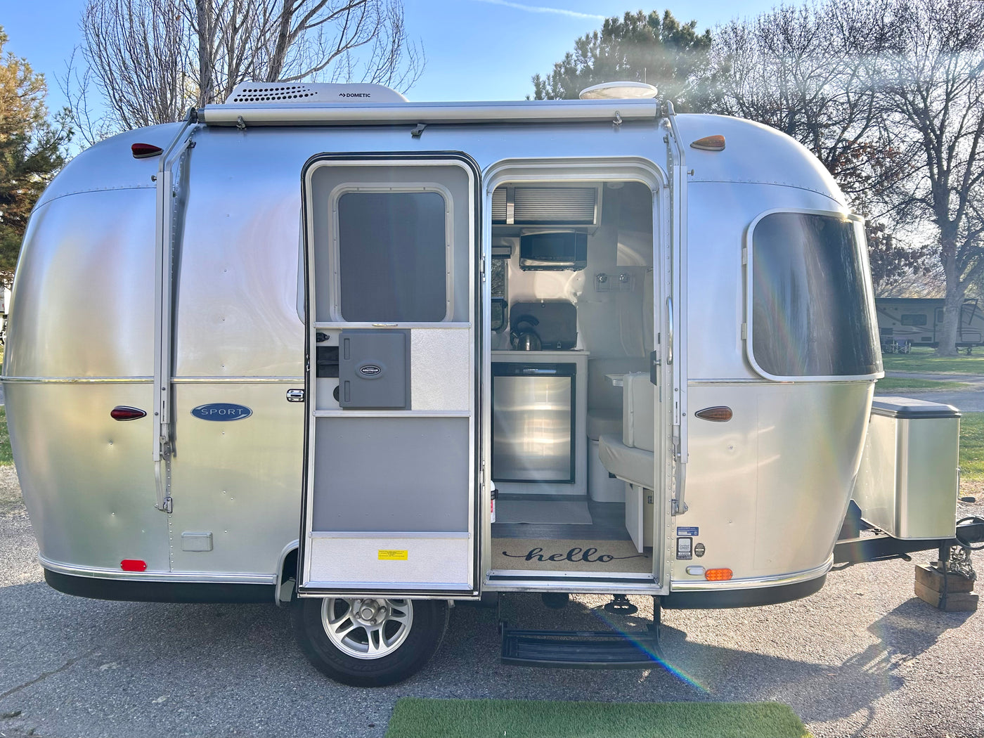 Shiny silver Airstream RV rental travel trailer with door open, revealing bright interior kitchen and dining area at a campsite. — photo 7
