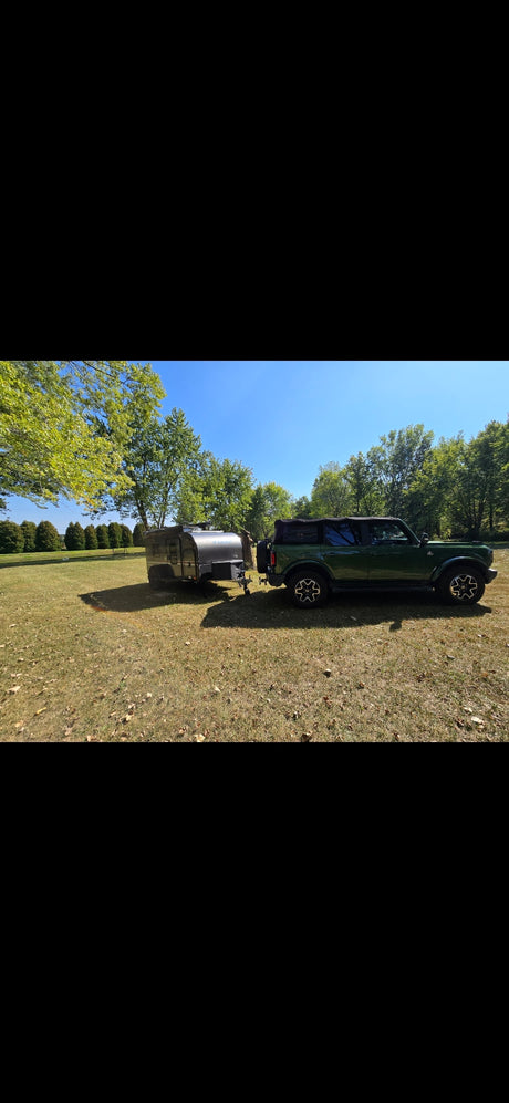 Green Bronco towing an **rv rental** (gray camper) in a sunny field for adventure.
