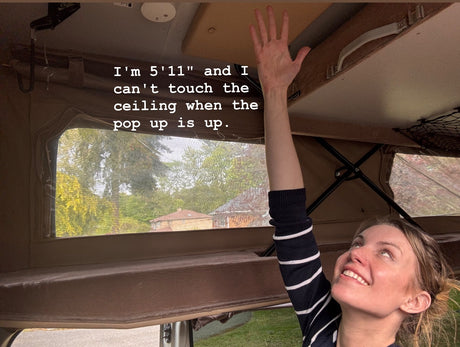 Woman at 5'11" reaches for the high ceiling in a pop-up RV rental, demonstrating ample headroom when extended.
