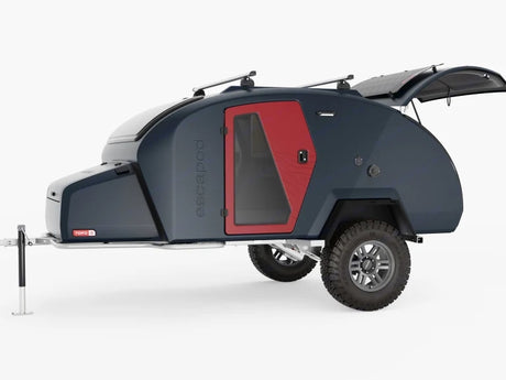 Compact, dark teardrop trailer with red door and roof racks, perfect rv rental for rugged outdoor escapades.