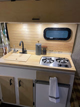 Modern RV rental kitchen setup with a black faucet, sink, two-burner stove, and light wood cabinetry for compact living.