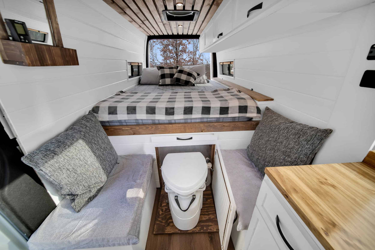 Cozy RV rental interior with a comfortable bed, custom wood accents, and a clever built-in toilet for van life adventures. — photo 7
