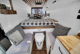 Cozy RV rental interior with a comfortable bed, custom wood accents, and a clever built-in toilet for van life adventures.