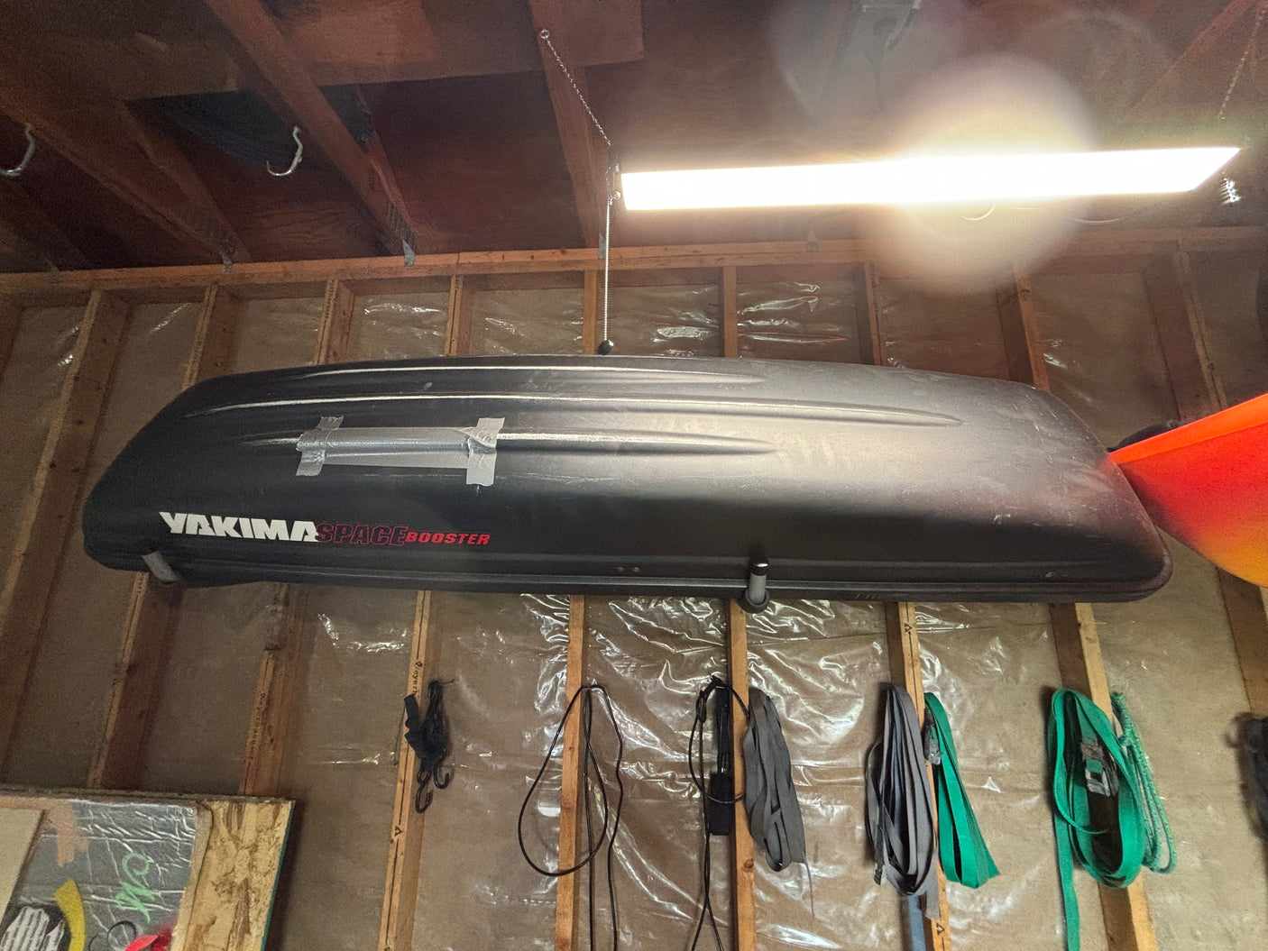 A large black Yakima SpaceBooster cargo box hangs from exposed wooden beams in a garage, ideal for RV rental trips.
