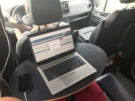 Working inside an rv rental (Mercedes van) on an HP laptop, with a charging phone, creating a mobile office on the go.