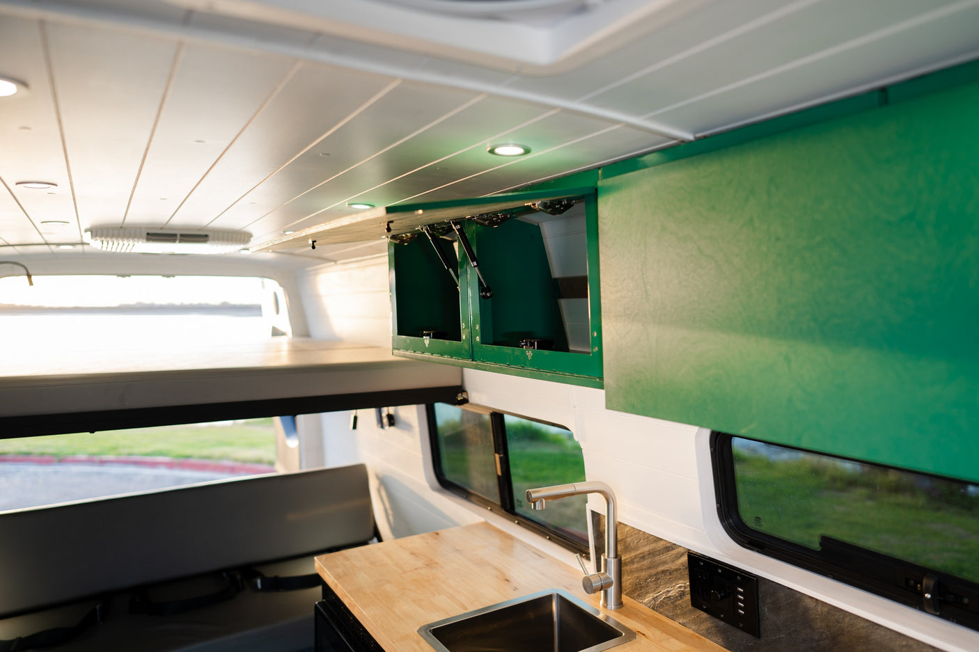 Inside this RV rental: bright ceiling, green cabinets (some open), wood counter with sink, and rear bunk area.
