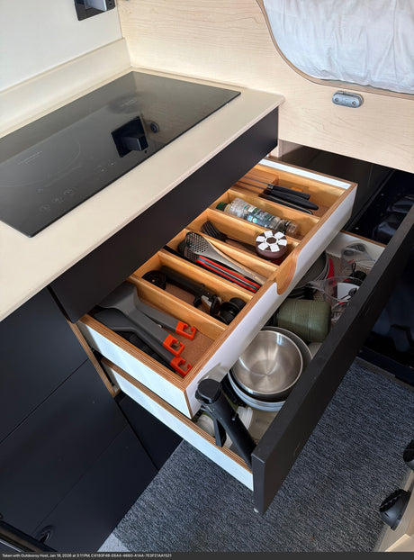 RV rental kitchen with organized pull-out drawers. Features an induction cooktop, cooking utensils, spices, and camping bowls.