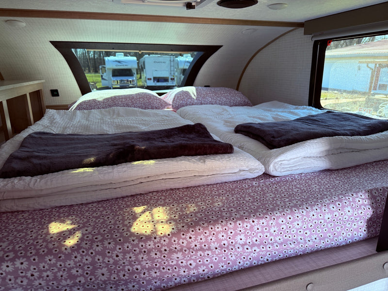 A comfortable RV rental interior showing a bed with floral sheets and white duvets, offering views of other RVs outside. — photo 2