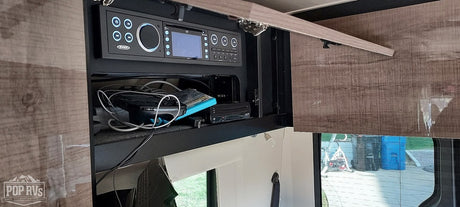 RV rental interior featuring a JENSEN stereo/control panel, storage cubby with devices, and wood-grain cabinet.