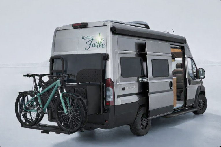 "Rolling Faith" gray RV rental with bikes on a rear rack, side door open, ready for outdoor adventures.