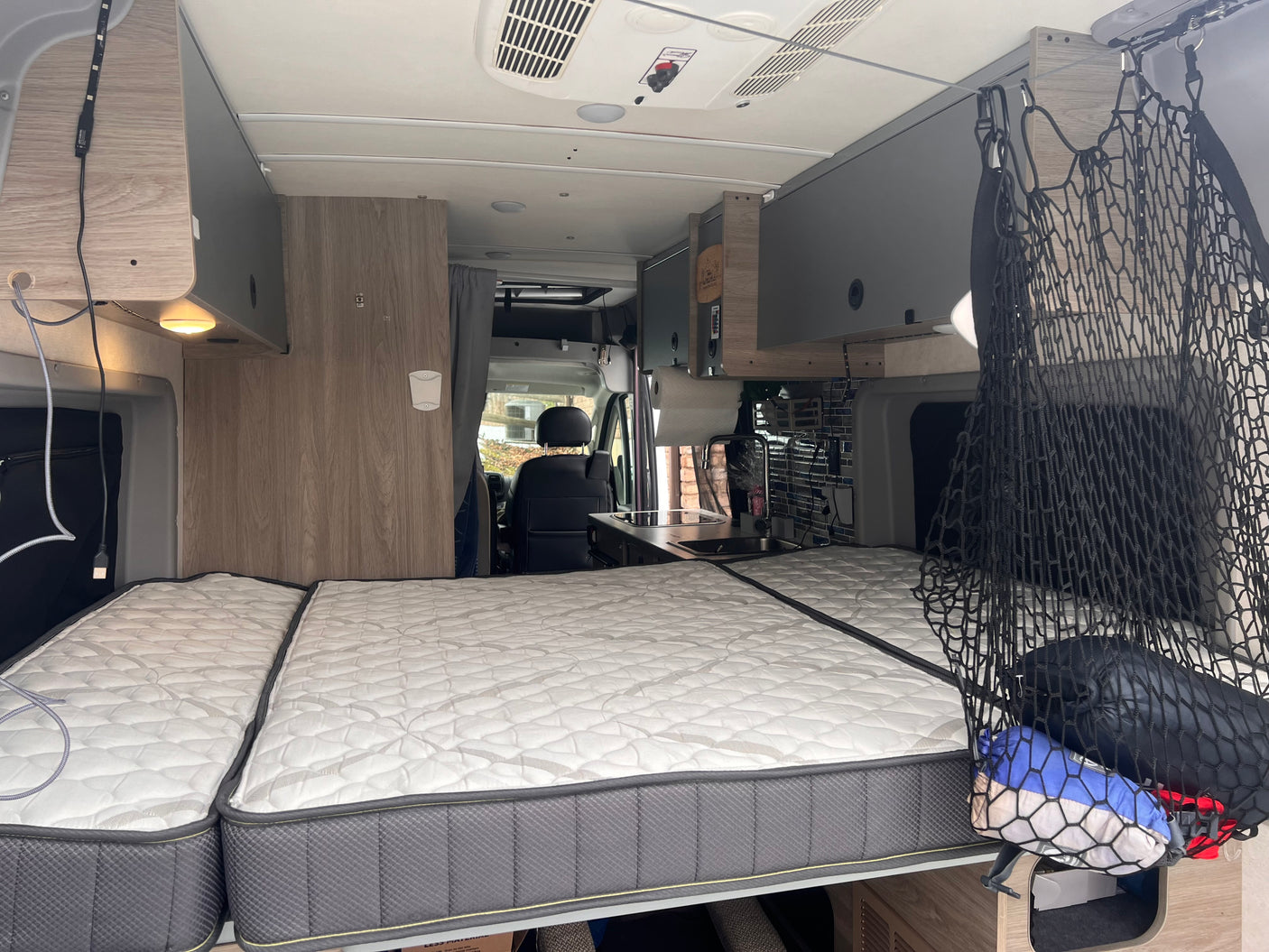 Cozy RV rental interior with bed, kitchenette, & overhead storage for comfortable travels.
