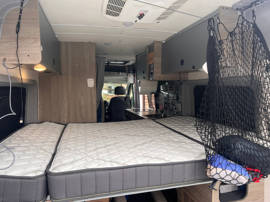 Cozy RV rental interior with bed, kitchenette, & overhead storage for comfortable travels.
