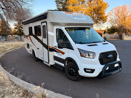 White Ford Transit motorhome rv rental with stylish brown graphics, bull bar, parked on asphalt.