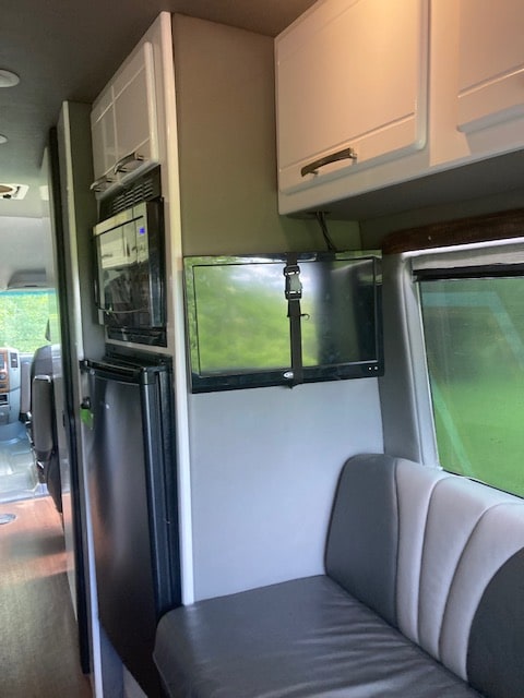 RV rental interior features a kitchenette with microwave/fridge, mounted TV, and striped bench seating. — photo 18