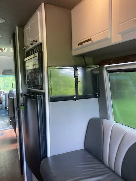 RV rental interior features a kitchenette with microwave/fridge, mounted TV, and striped bench seating.