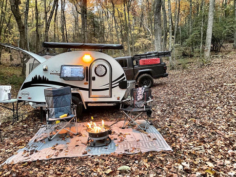 Fall **rv rental** adventure: Teardrop camper & truck in a scenic forest campsite with a cozy campfire & autumn leaves.