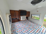 RV rental bedroom view: Featuring a fun, patterned bed, TV, AC unit, stereo system, and a window looking outdoors.