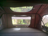 Interior of an RV rental rooftop tent. Enjoy nature views from this cozy camping setup with a comfy mattress.