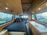 Bright, custom camper van interior, available for RV rental. Features wood accents, versatile seating, and a mini-kitchen.