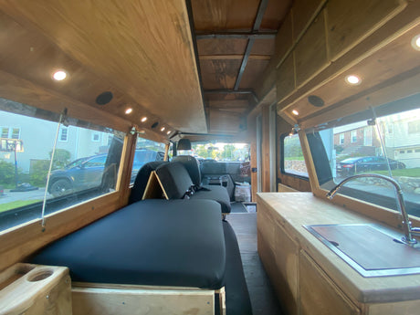 Bright, custom camper van interior, available for RV rental. Features wood accents, versatile seating, and a mini-kitchen.