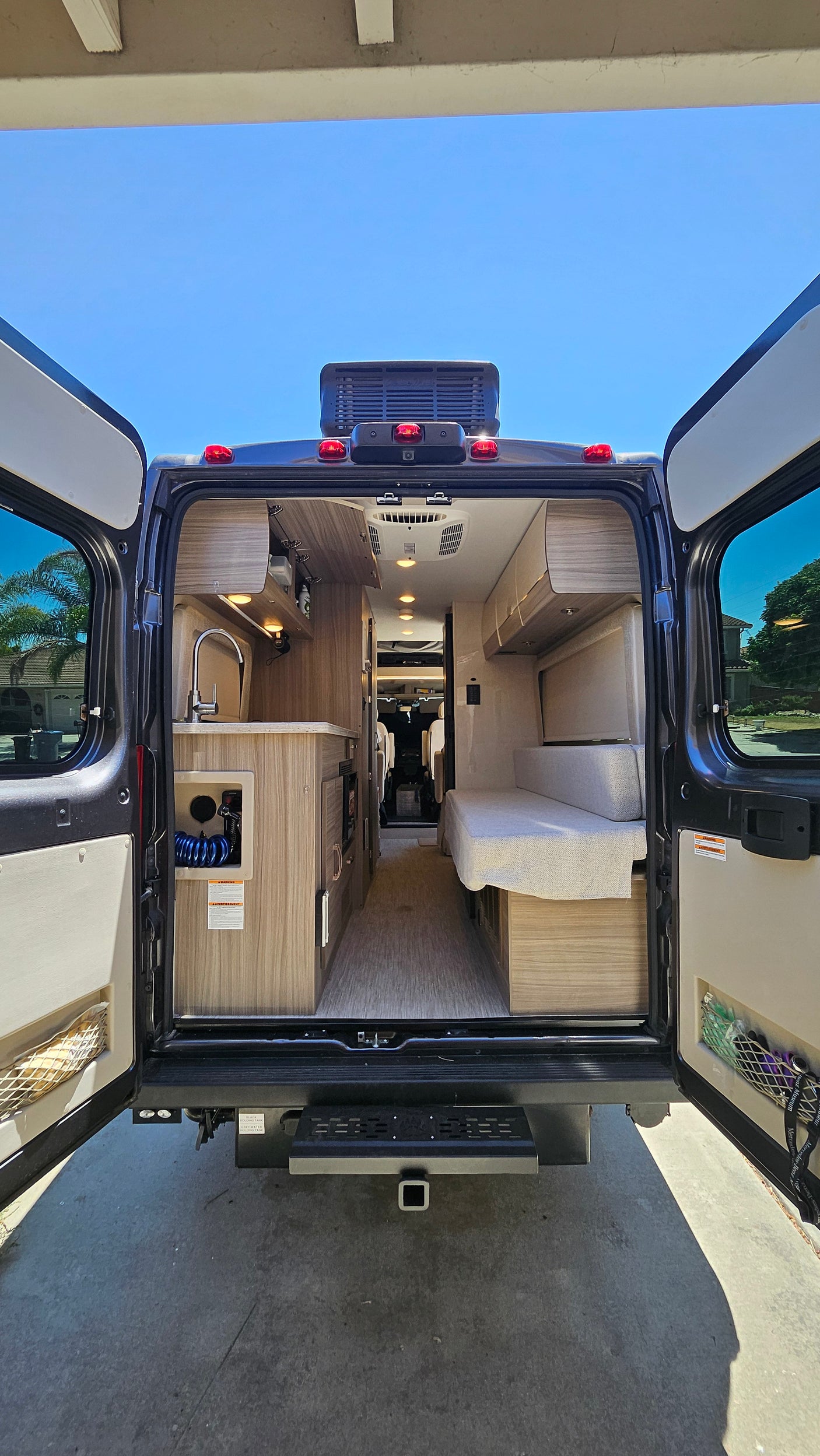 Inside an RV rental: rear doors open, revealing a modern interior with a kitchen, living space, and wood accents.