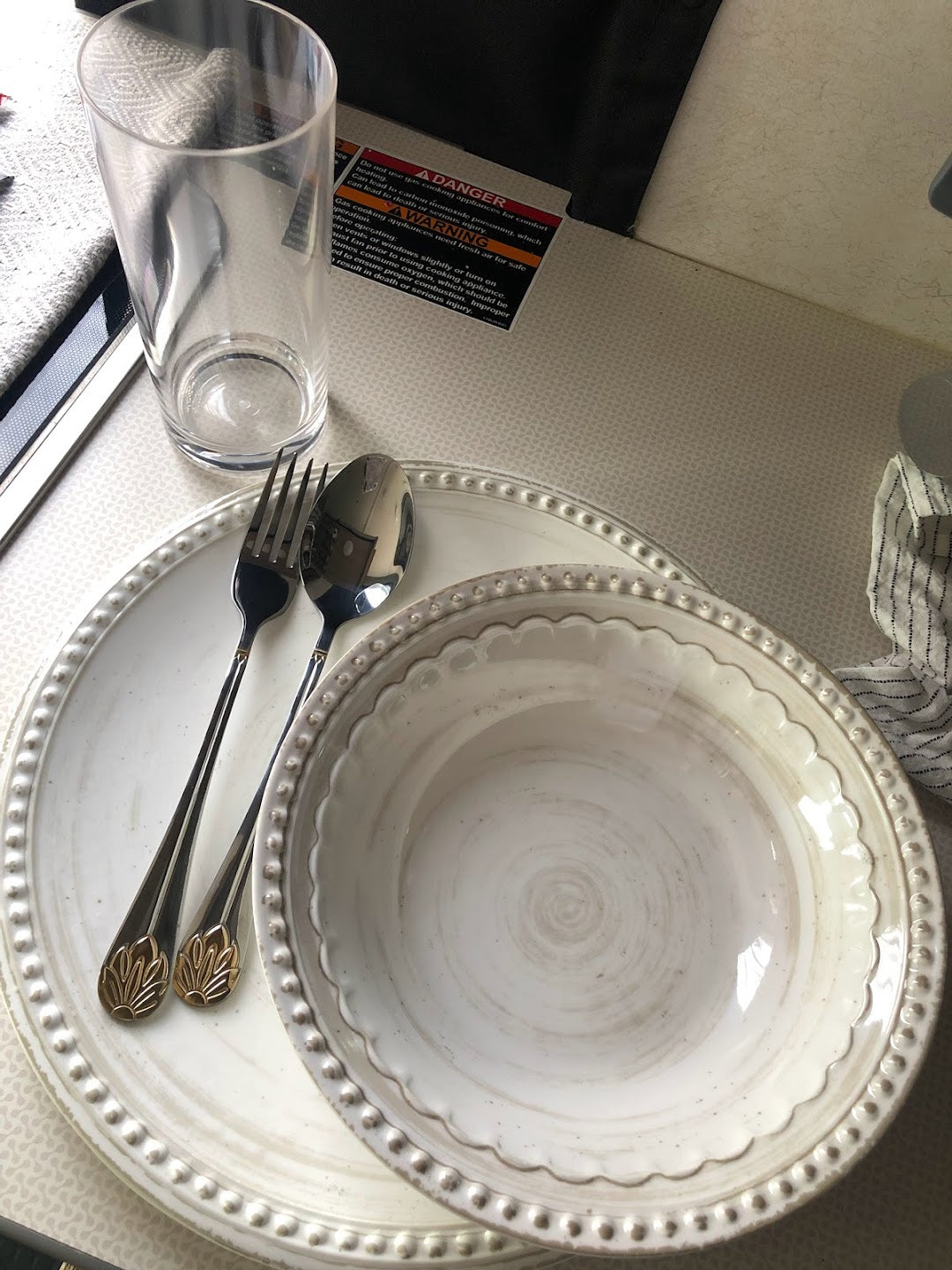 RV rental dining setup: Beaded plates, utensils, glass on a patterned counter with appliance safety warnings.