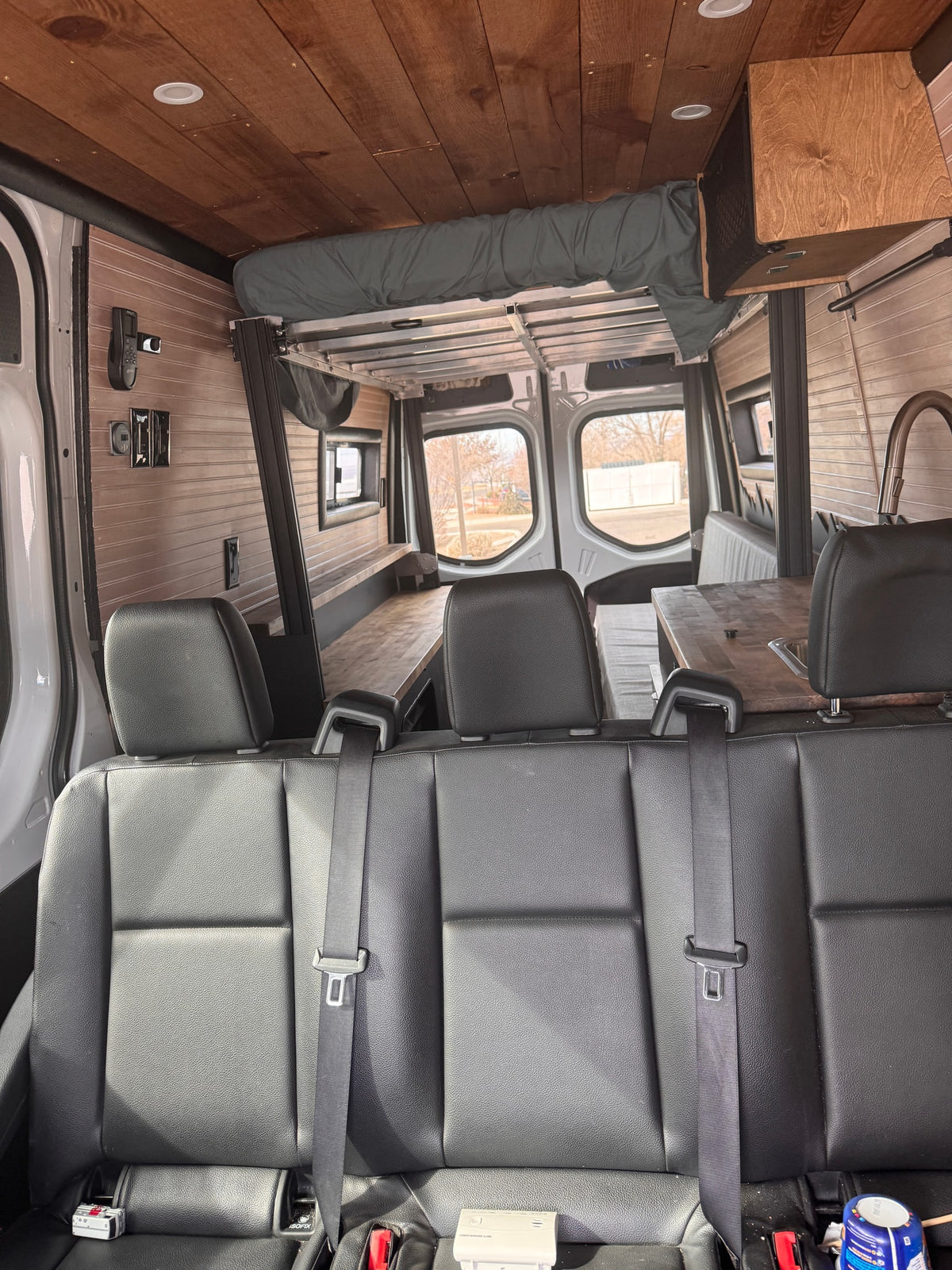 Inside this customized rv rental, a comfortable camper van interior with wood paneling, a versatile bed, and kitchen setup. — photo 2