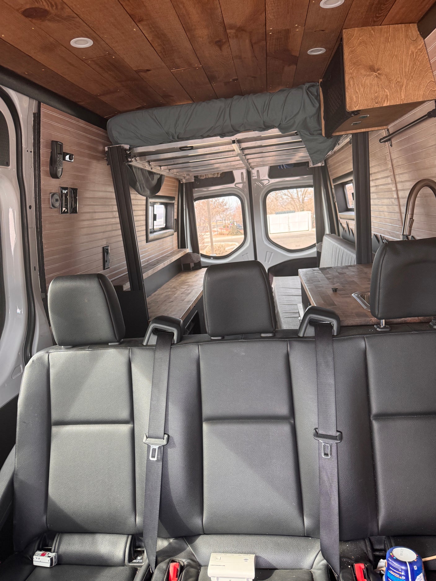 Inside this customized rv rental, a comfortable camper van interior with wood paneling, a versatile bed, and kitchen setup.