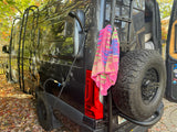 This RV rental camper van features an outdoor shower, side ladder, and rear spare tire, surrounded by autumn leaves.