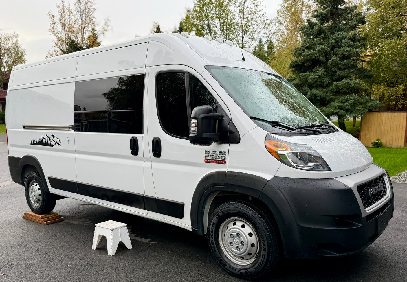 A white Ram Promaster RV rental, equipped as a camper van, parked on leveling blocks outdoors.