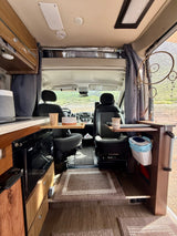 Cozy rv rental interior with a mobile workstation, compact kitchen, and swiveling front seats, perfect for a road trip.