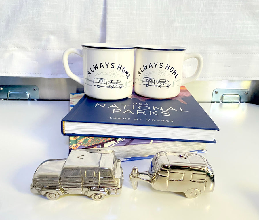Travel-themed decor: 'Always Home' mugs with car/RV graphics, a National Parks book, and silver car/RV shakers. Great for rv rental enthusiasts.