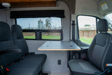 This RV rental's interior features versatile seating, a foldable table, and large windows revealing scenic outdoor views.