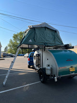 This RV rental setup features a teardrop camper with a large rooftop tent & ladder, ready for adventure camping.