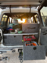RV rental rear view: well-equipped SUV camping setup with cooking gear and storage drawers, ideal for overland adventures at sunset.