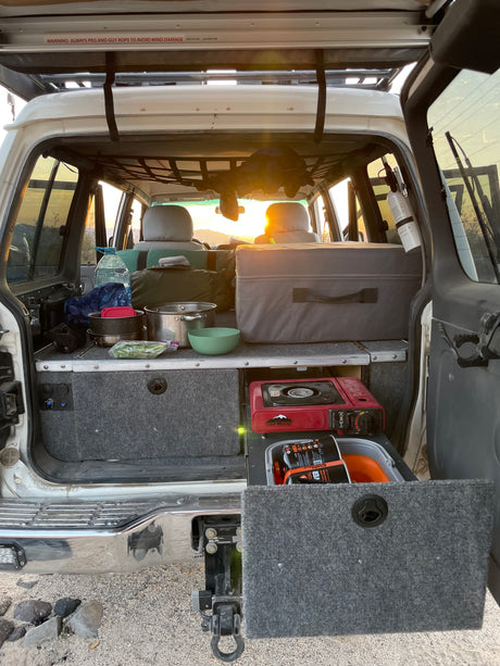 RV rental rear view: well-equipped SUV camping setup with cooking gear and storage drawers, ideal for overland adventures at sunset.